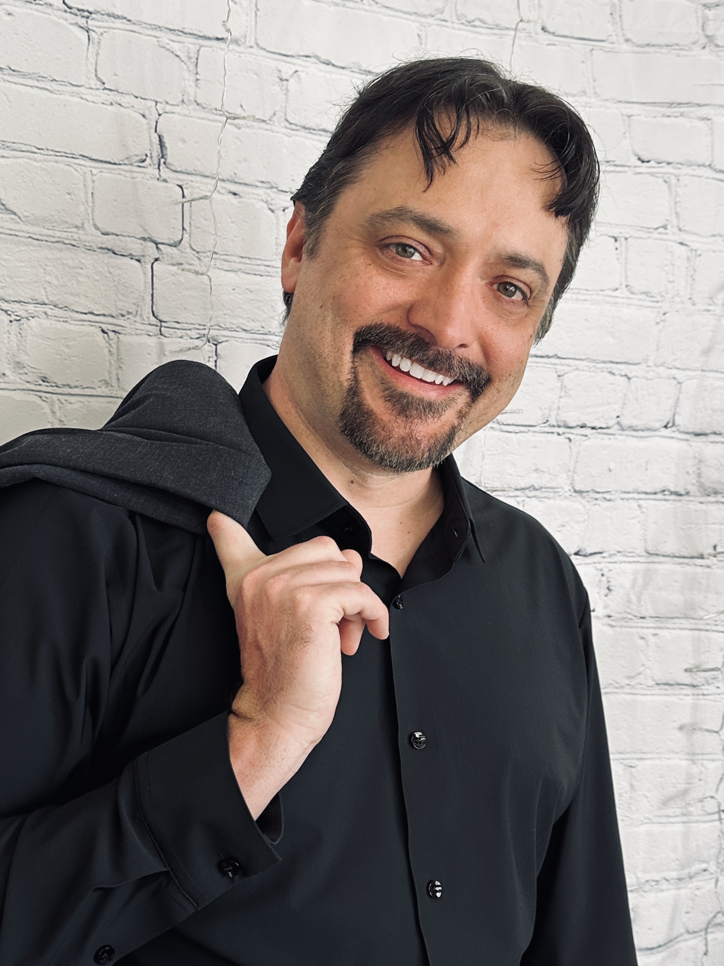 Rickie Lee Tanner smiling in a black shirt against a white brick wall